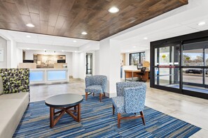 A hotel lobby with a reception desk, seating area with patterned chairs, a round table, and a large window with a view of the street. - Holiday Inn Express Hopewell - Fort Lee by IHG (Hopewell)