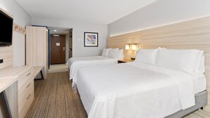 Une chambre d’hôtel avec deux lits, un bureau, une télévision et une tête de lit en bois.