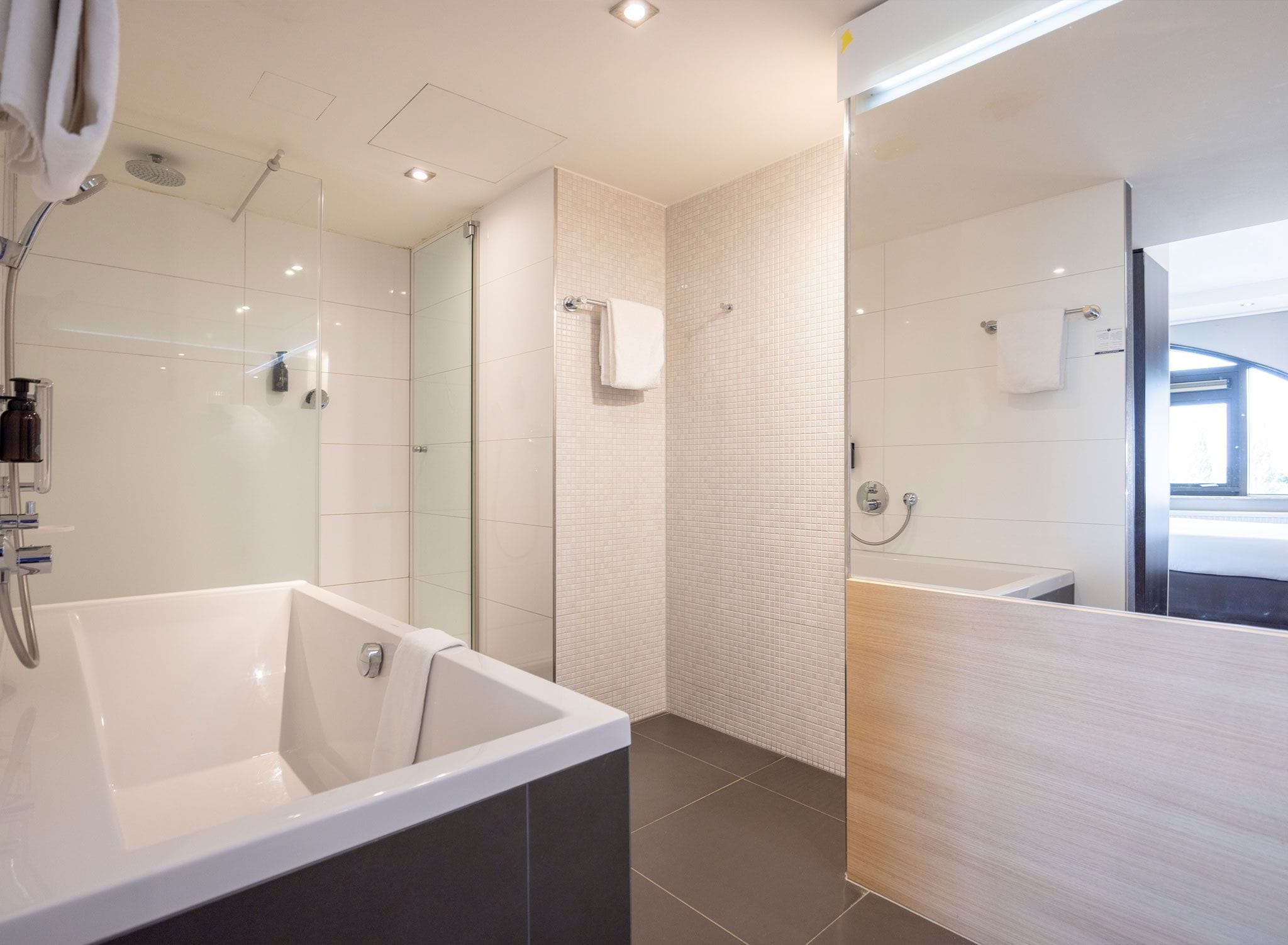 Un baño moderno con una bañera grande, un box de ducha de vidrio y un tocador de madera.