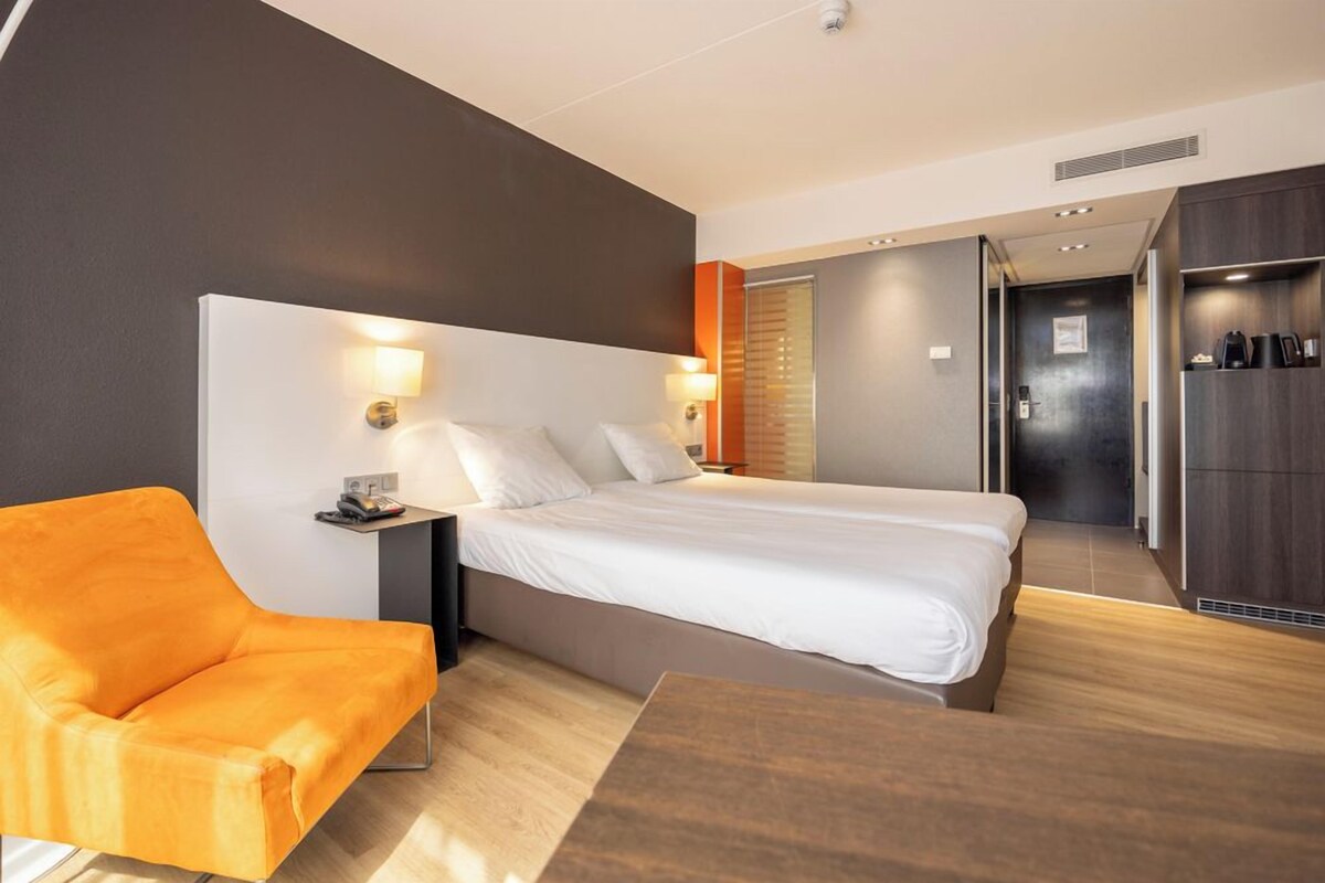Une chambre d’hôtel moderne équipée d’un lit, d’une table de chevet, d’une lampe, d’une chaise et d’une armoire.