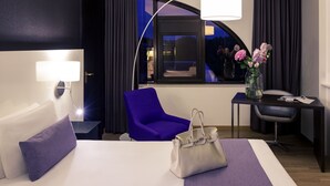 Habitación de hotel con cama, escritorio, silla, lámpara y ventana con cortinas.