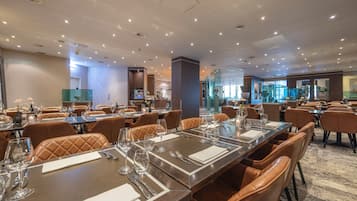 Un comedor de hotel con varias mesas dispuestas para comer, equipado con cubiertos y vasos.