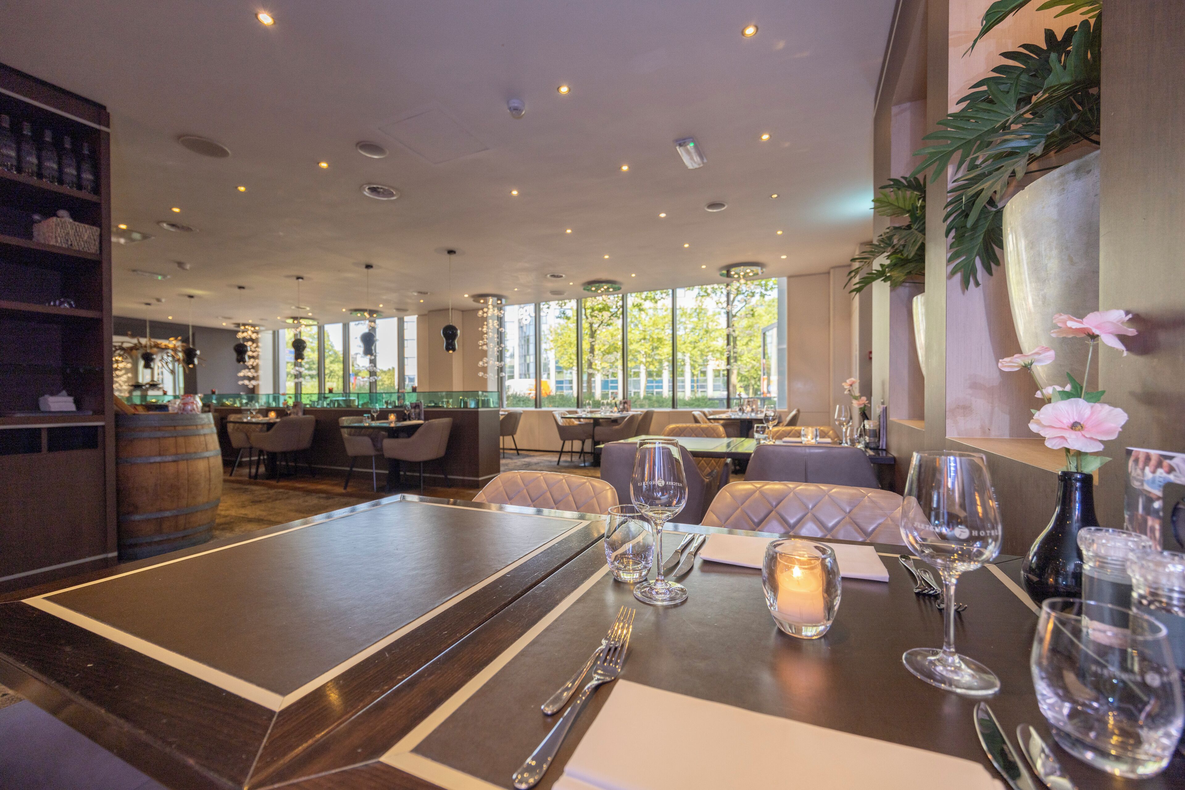 A restaurant interior with a long dining table, chairs, and a bar area with shelves and a barrel.