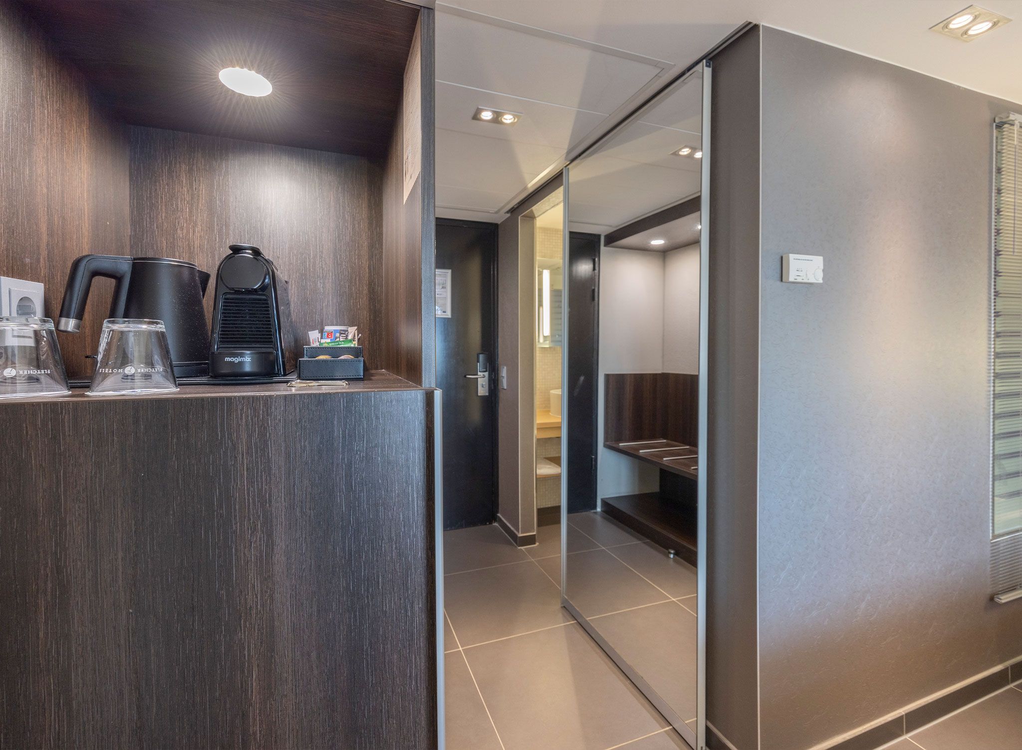 A modern hotel room with a dark wood finish, a coffee machine, and a kettle on a counter.