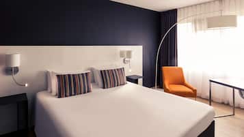 A modern hotel room with a large bed, two bedside tables, a chair, and a desk.