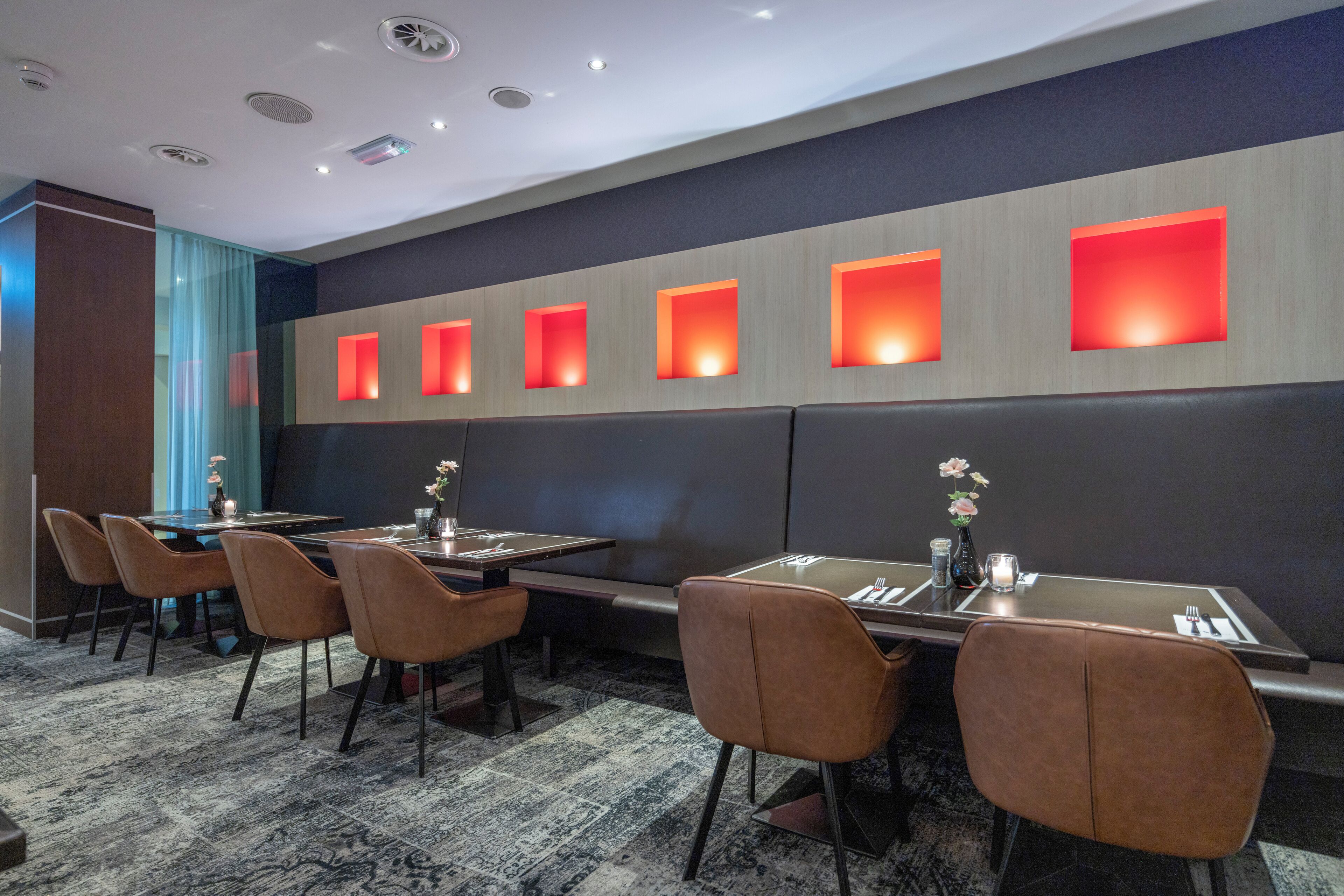 A modern hotel room with a long dining table, multiple chairs, and a row of illuminated wall panels.