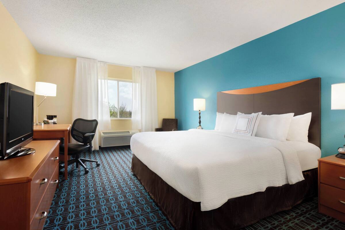 A hotel room with a large bed, a desk with a computer, a TV, and a chair.