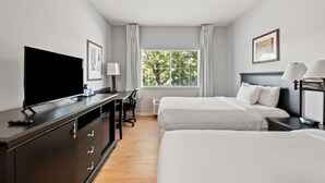 A hotel room with a TV, desk, two beds, a window with curtains, and a framed picture on the wall. - Willow Inn Suites Rochester (Rochester)