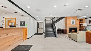 A modern hotel lobby with a wooden reception desk, a staircase, a fireplace, and a seating area. - Willow Inn Suites Rochester (Rochester)