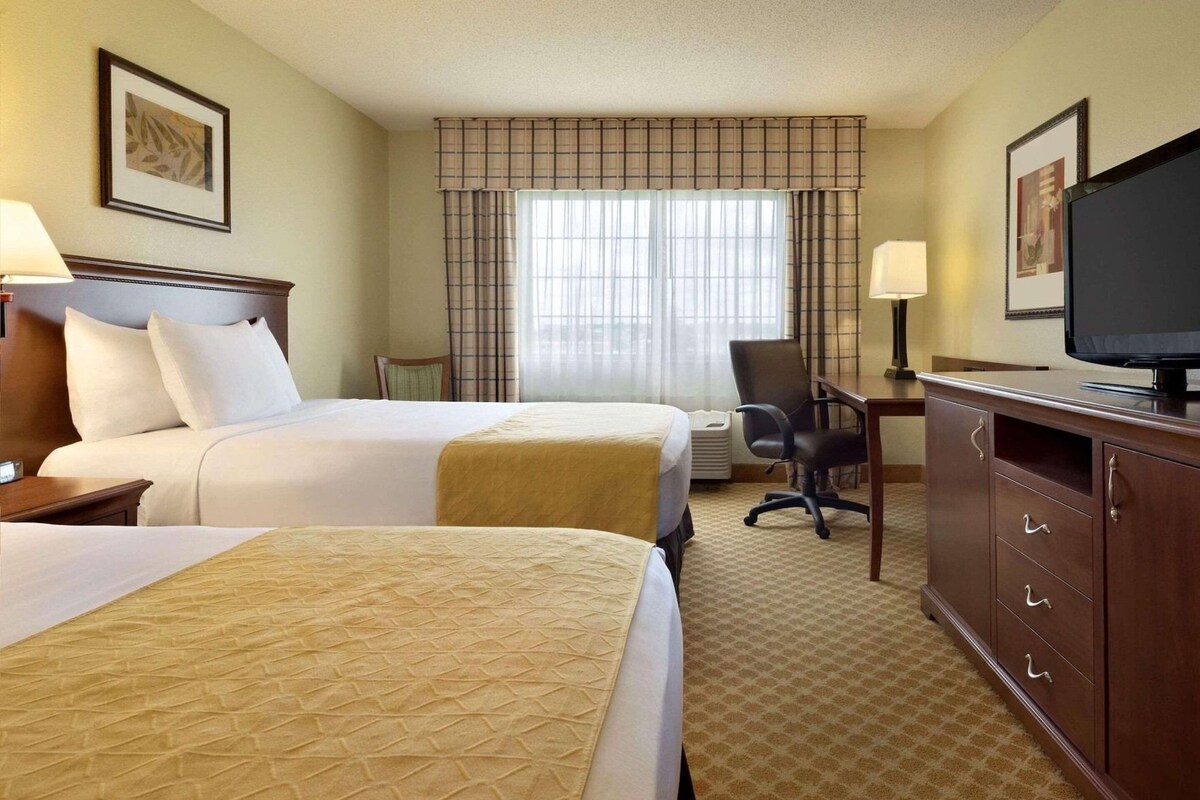 A hotel room with two beds, a desk, a chair, a television, and a window with curtains.