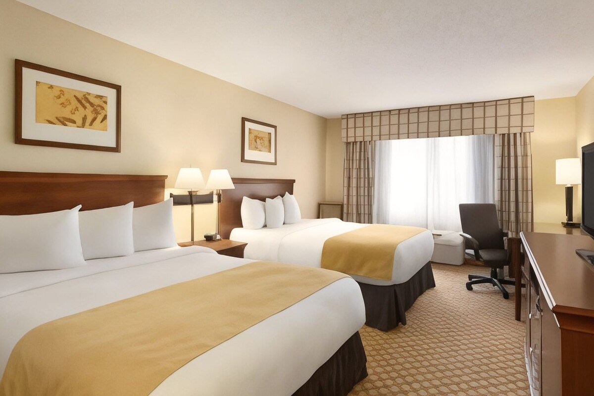 A hotel room with two beds, a desk, a chair, and a television.