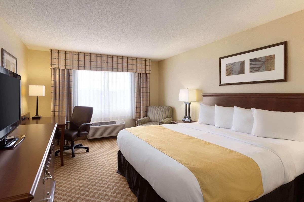 A hotel room with a bed, a desk with a TV, a chair, a lamp, and a window with curtains.
