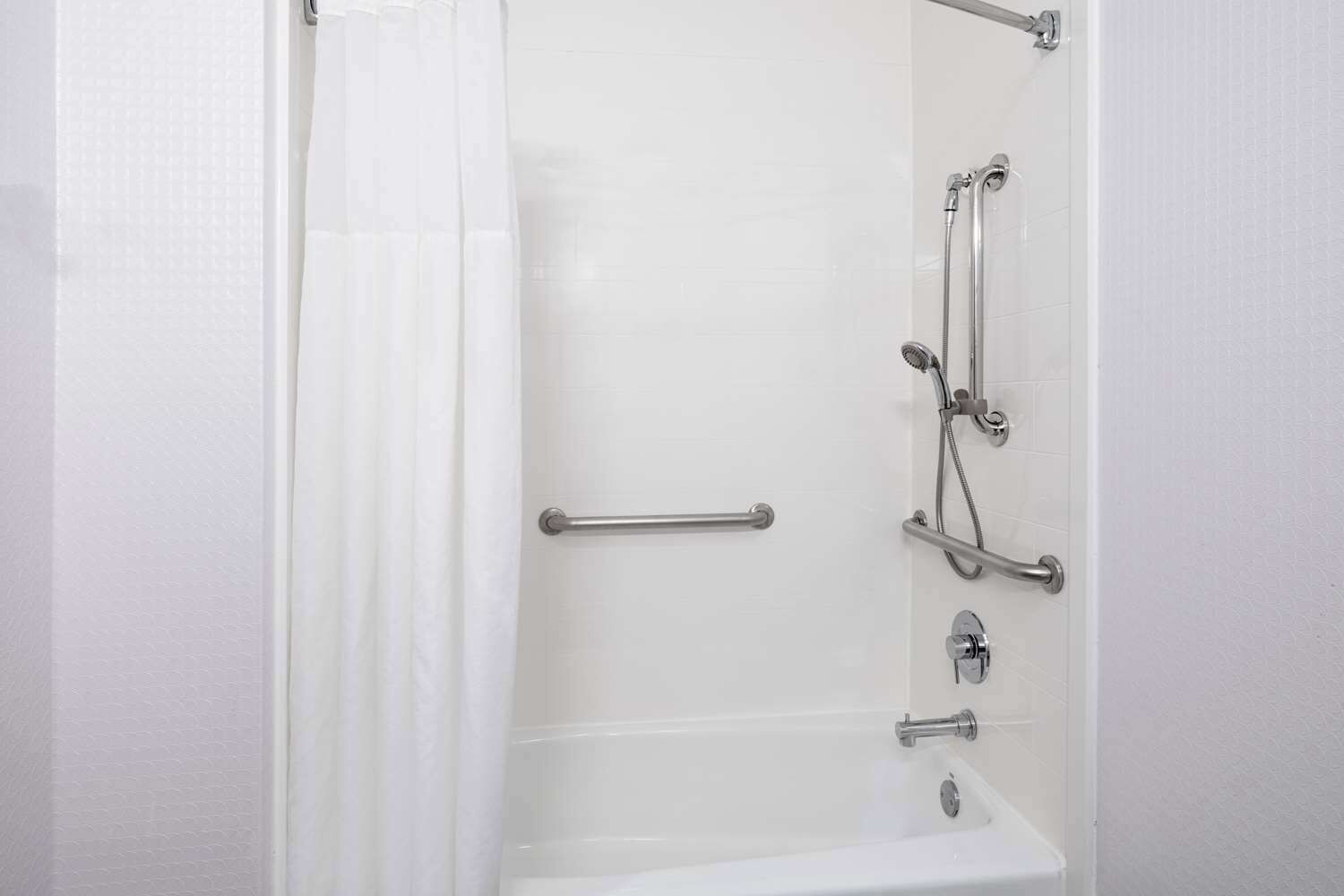 A bathroom with a bathtub, grab bars, and a showerhead.