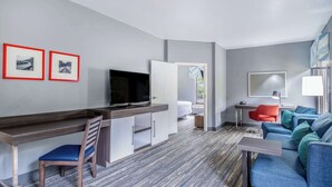 A modern hotel room with a desk, television, seating area, and artwork on the walls. - Hampton Inn Sanford (Sanford)