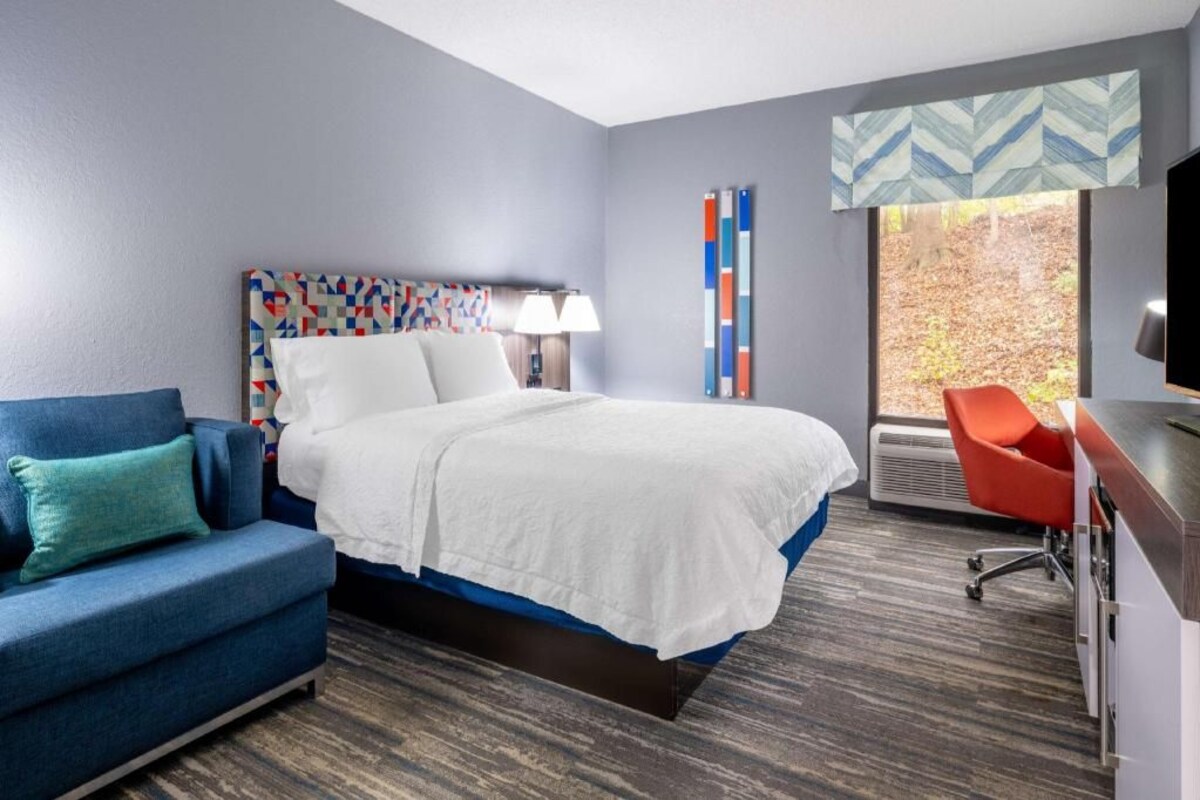 A hotel room with a bed, a blue sofa, a desk, and a window with a view of trees.