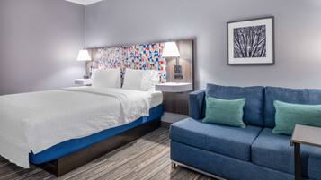 A hotel room with a bed, a blue sofa, a patterned headboard, and a framed picture on the wall.