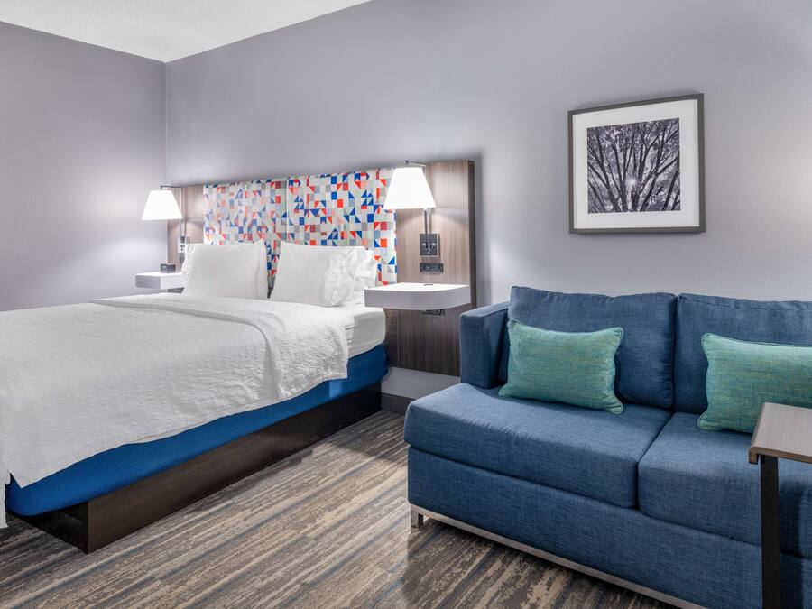 A hotel room with a bed, a blue sofa, a patterned headboard, and a framed picture on the wall.