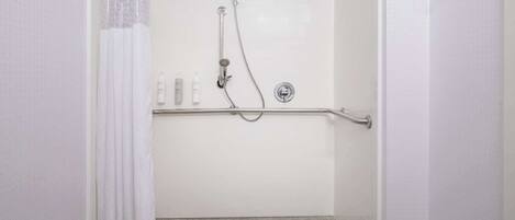 A shower with a grab bar, a white tiled wall, and a tiled floor.
