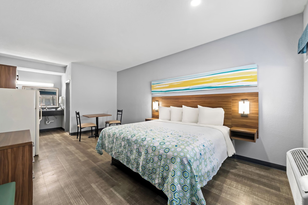 A hotel room with a large bed, a desk, a chair, and a small table.