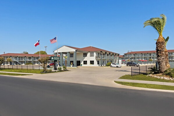 Un hotel con entrada central, varias banderas y una palmera.