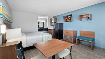 Een moderne hotelkamer met een bed, een bureau, een stoel, een bankje, een magnetron, een koelkast en een kapstok.