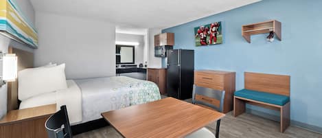 Una habitación de hotel moderna con una cama, un escritorio, una silla, un banco, un microondas, un refrigerador y un perchero de pared.