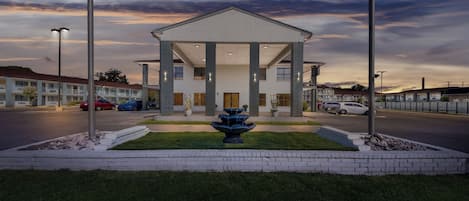 Un hotel con una fuente central, un acceso cubierto y un estacionamiento.