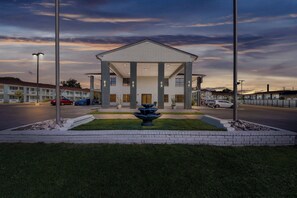 Un hotel con una fuente central, un acceso cubierto y un estacionamiento.