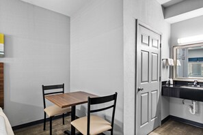A small, private bathroom with a wooden table and two chairs, a sink, and a mirror.