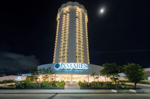 Un hotel alto con un llamativo letrero 'AMARES' en la entrada, que presenta un diseño moderno con varios balcones y una fachada bien iluminada.