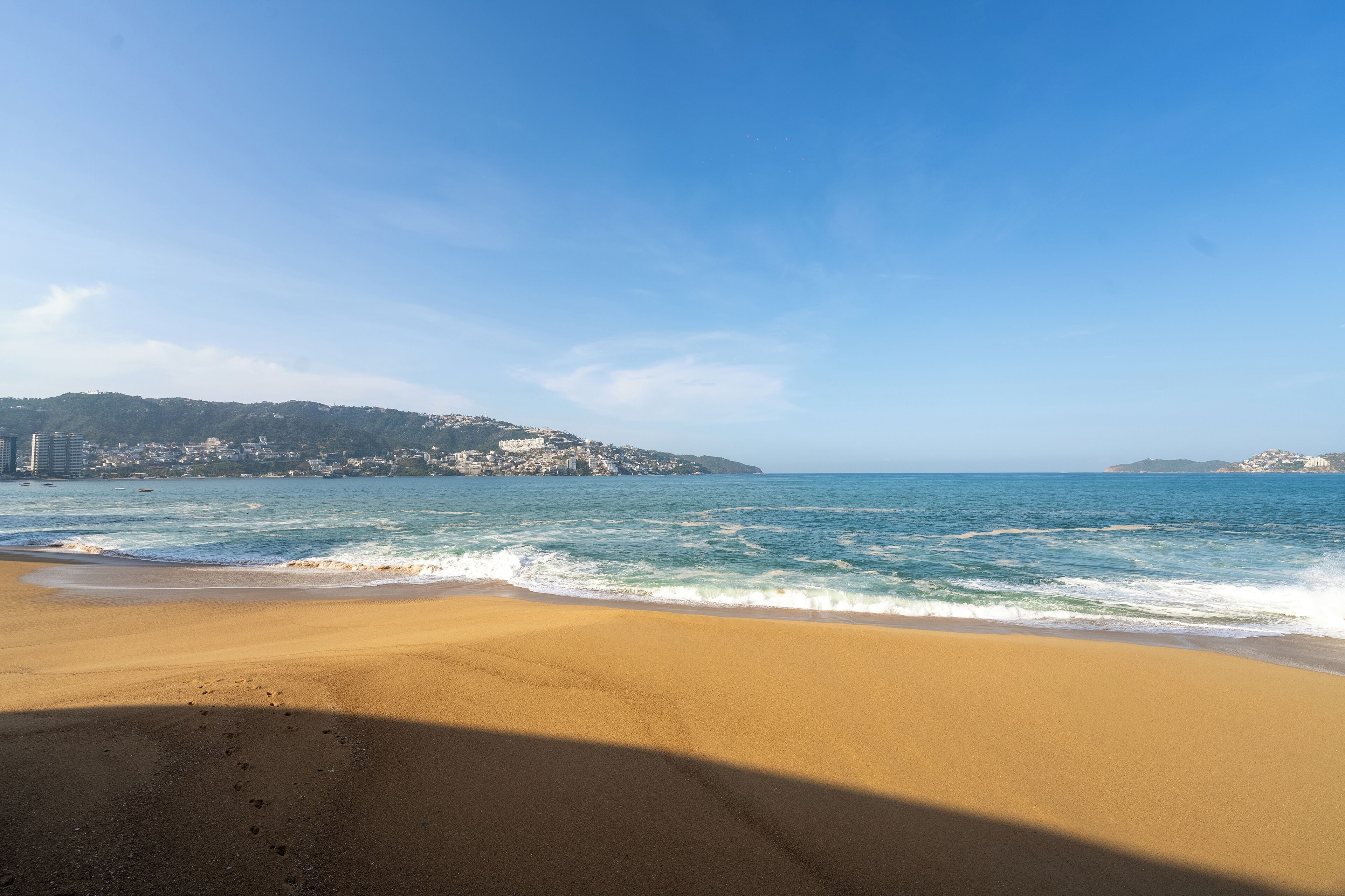 A beach with a clear view of the ocean and distant hills.