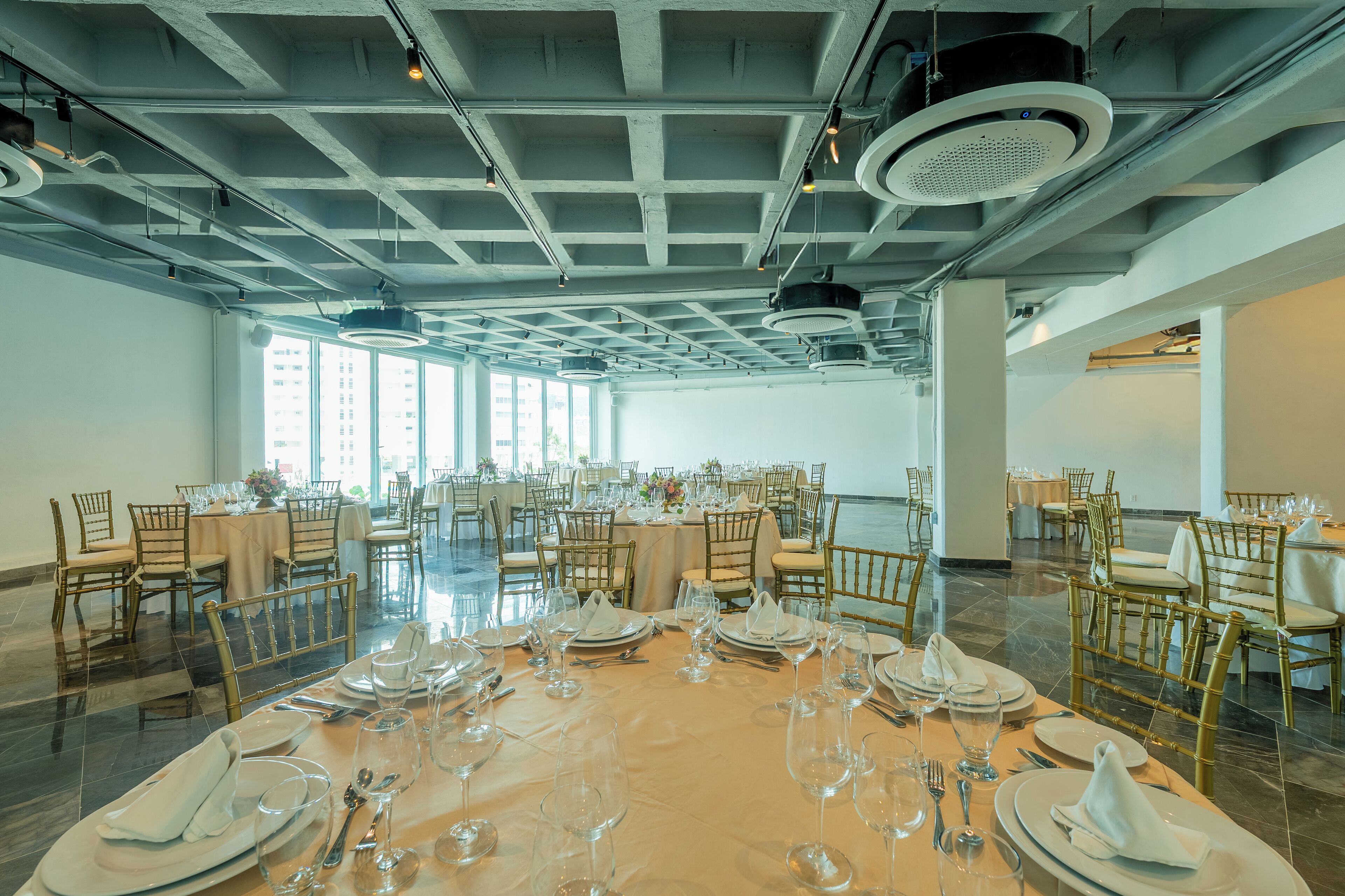 A spacious banquet hall with multiple round tables set for dining, featuring gold chairs and white tablecloths.