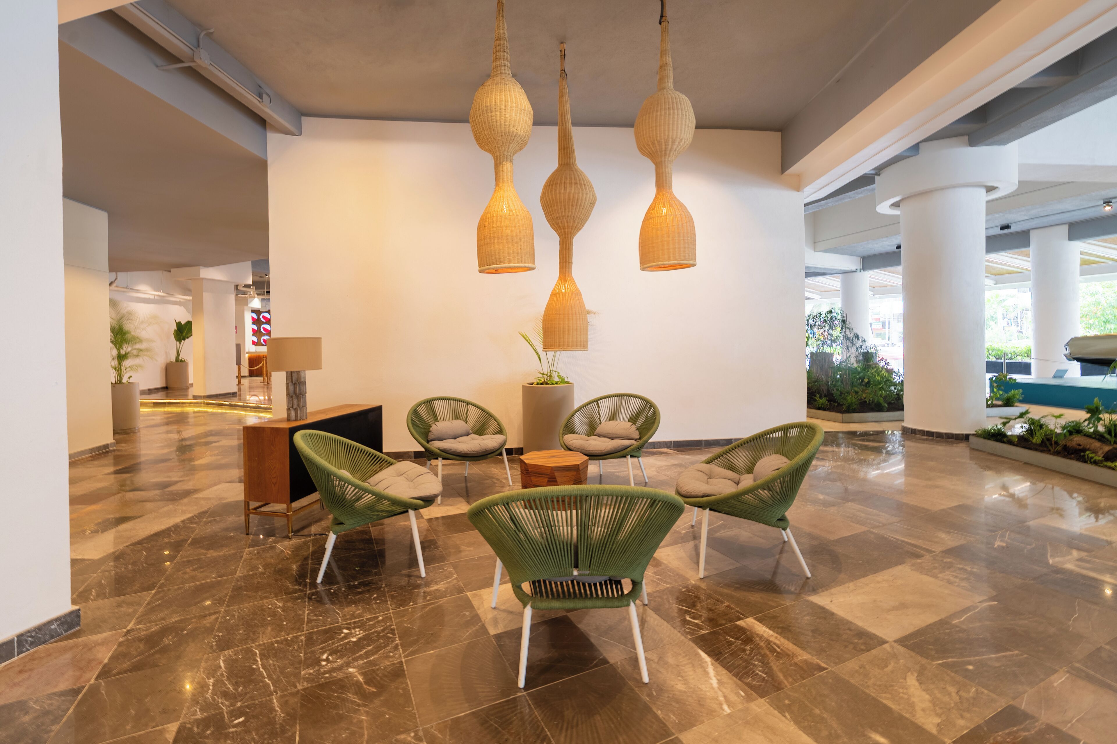 A lobby with a marble floor, green chairs, a wooden table, and hanging lamps.