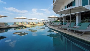 Zona de piscina amb gandules i ombrelles, cel serè i vista al mar.
