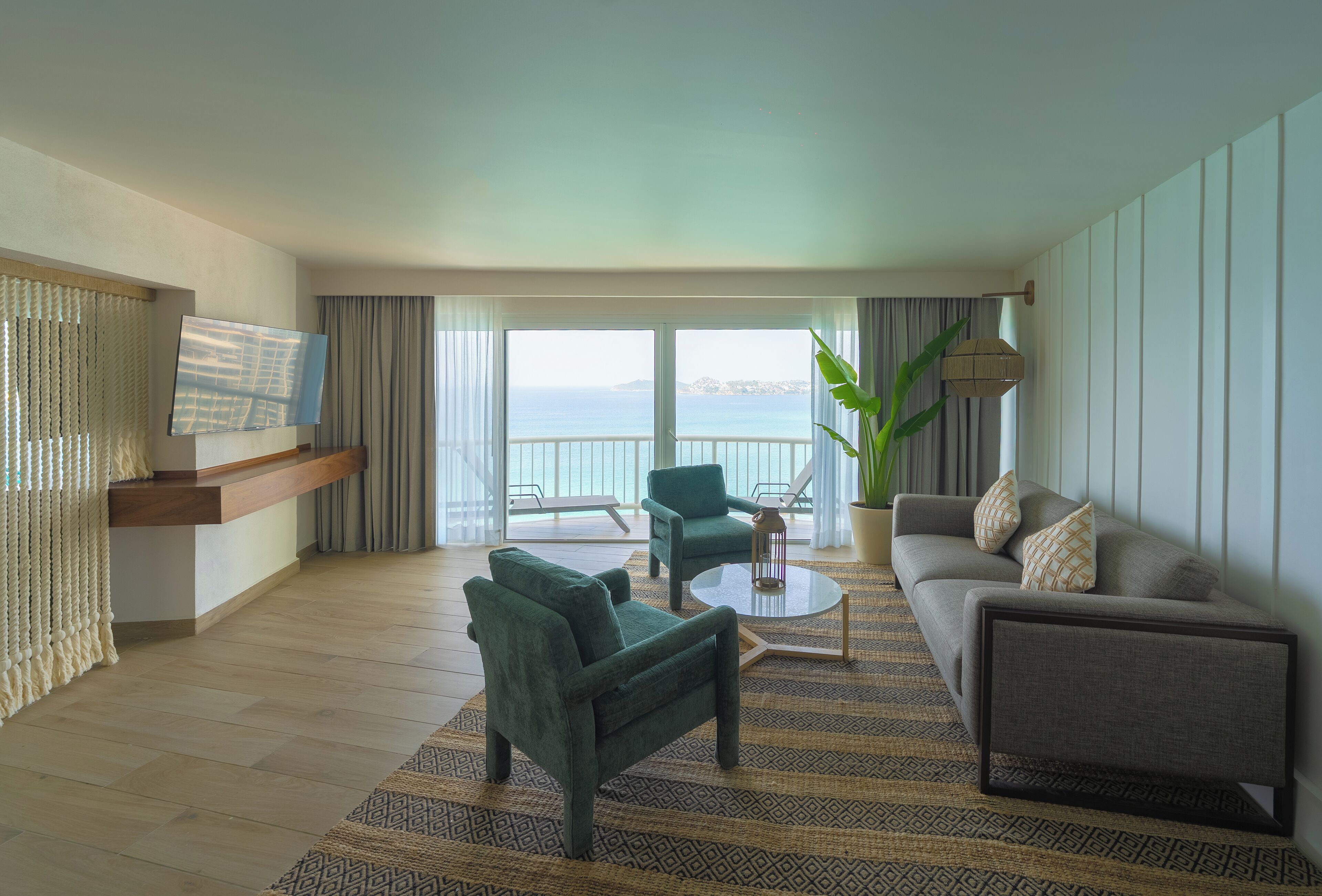 Une chambre d’hôtel moderne équipée d’un canapé, d’un fauteuil et d’un téléviseur posé sur un meuble.