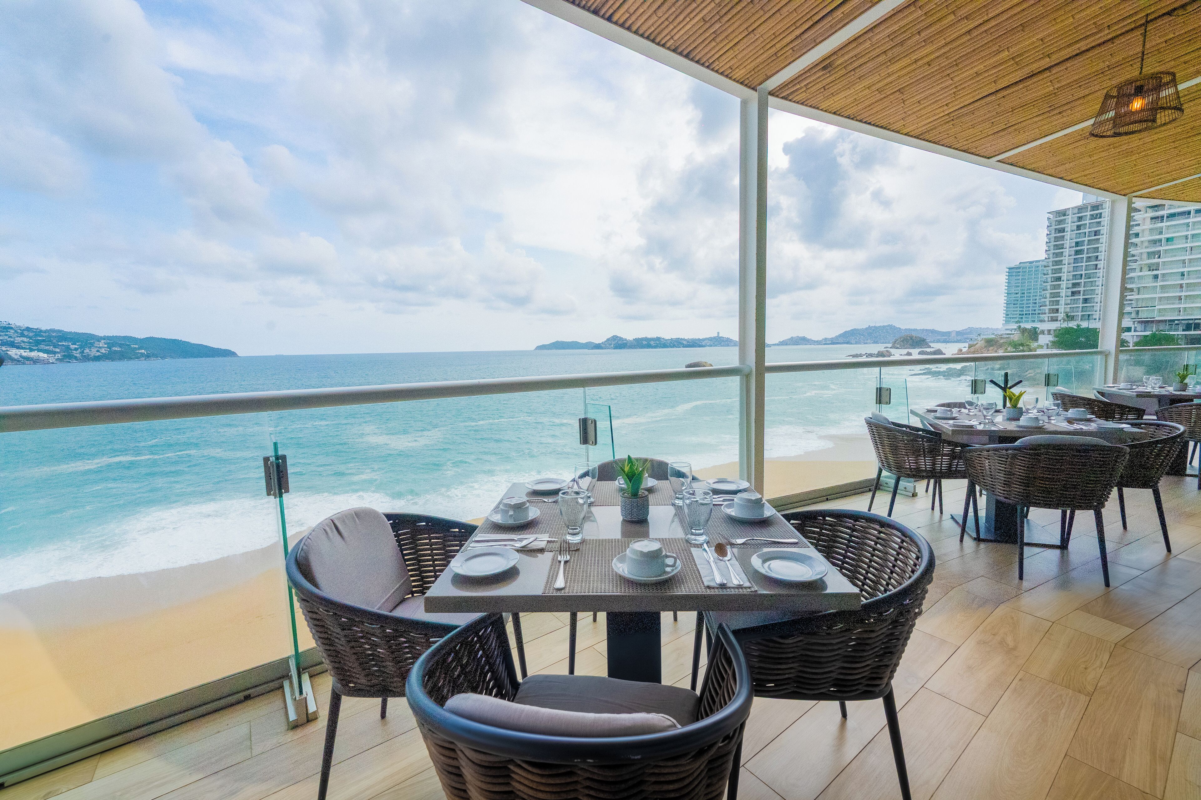 A restaurant with tables set for dining, overlooking a beach and ocean.