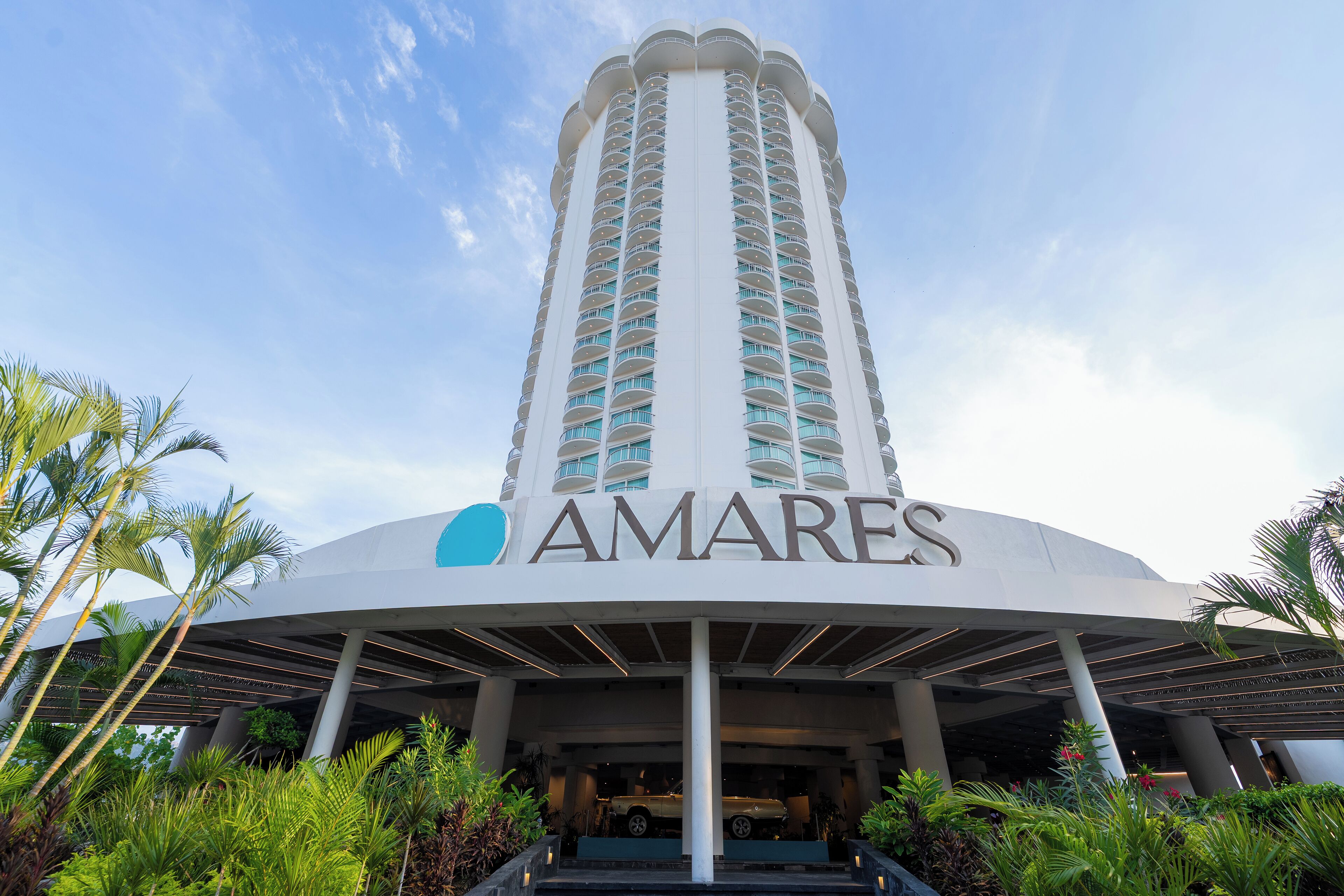 A tall hotel with a prominent 'AMARES' sign, featuring a modern design with a curved entrance and a central column.