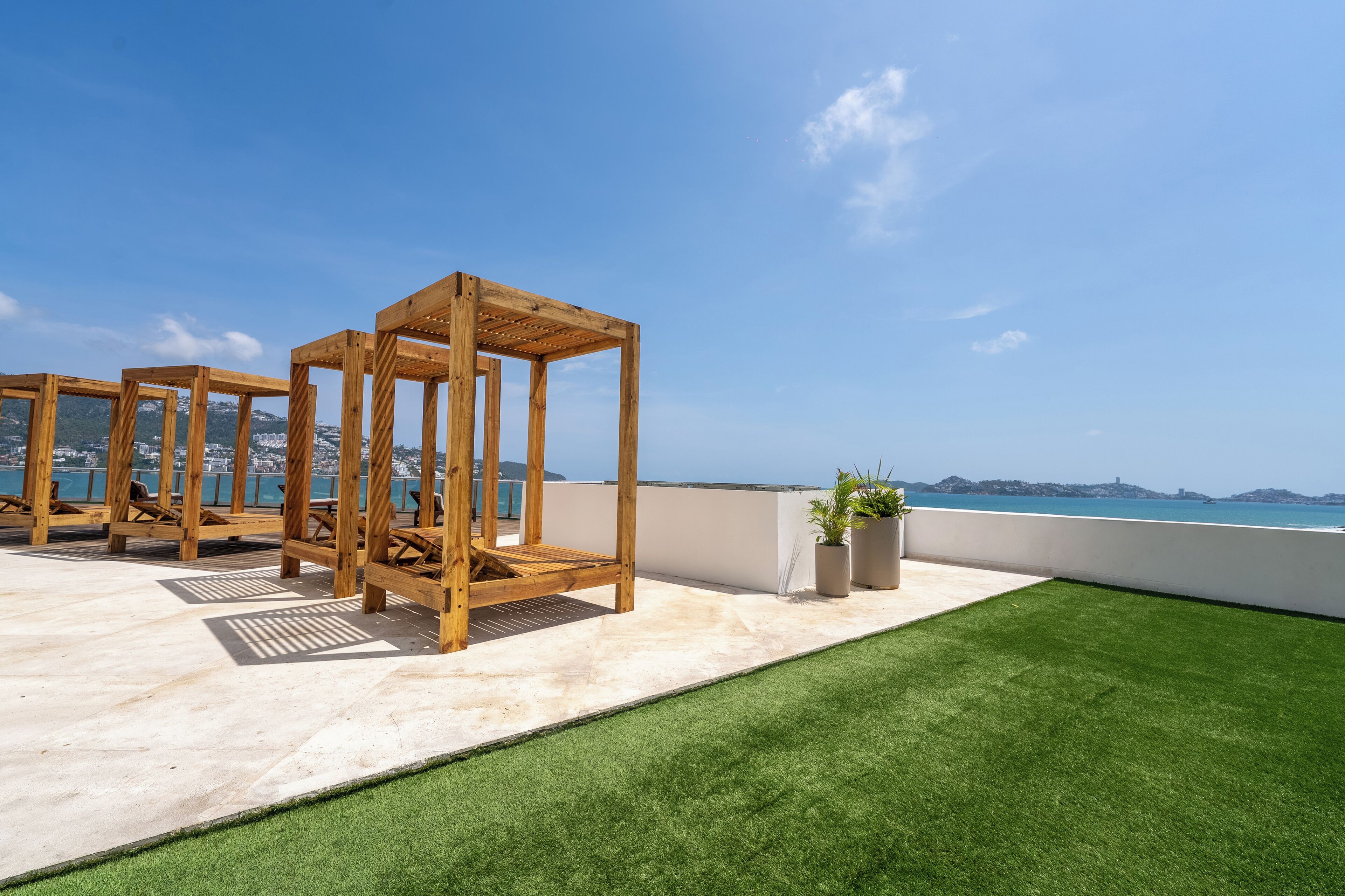 A rooftop terrace with wooden pergolas, artificial grass, and potted plants.