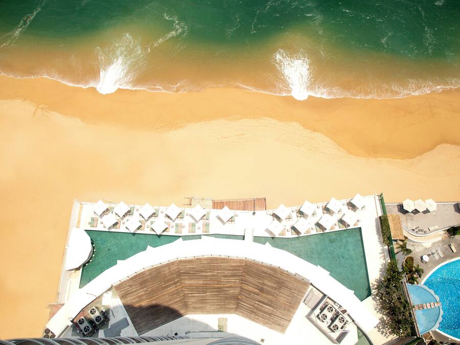 An aerial view of a beachside hotel with a swimming pool and sun loungers.