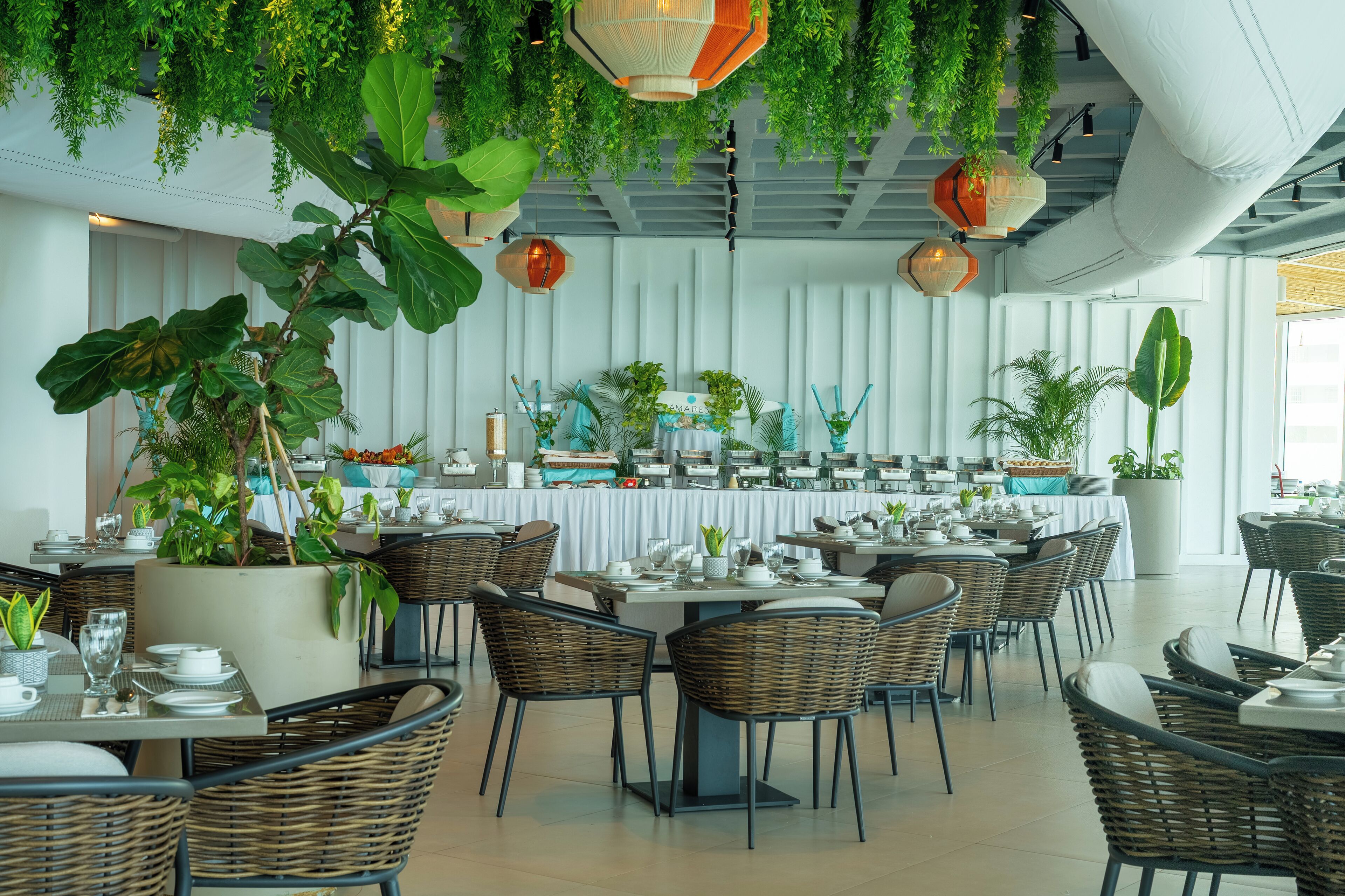 A restaurant with high ceilings, hanging plants, and wicker furniture.