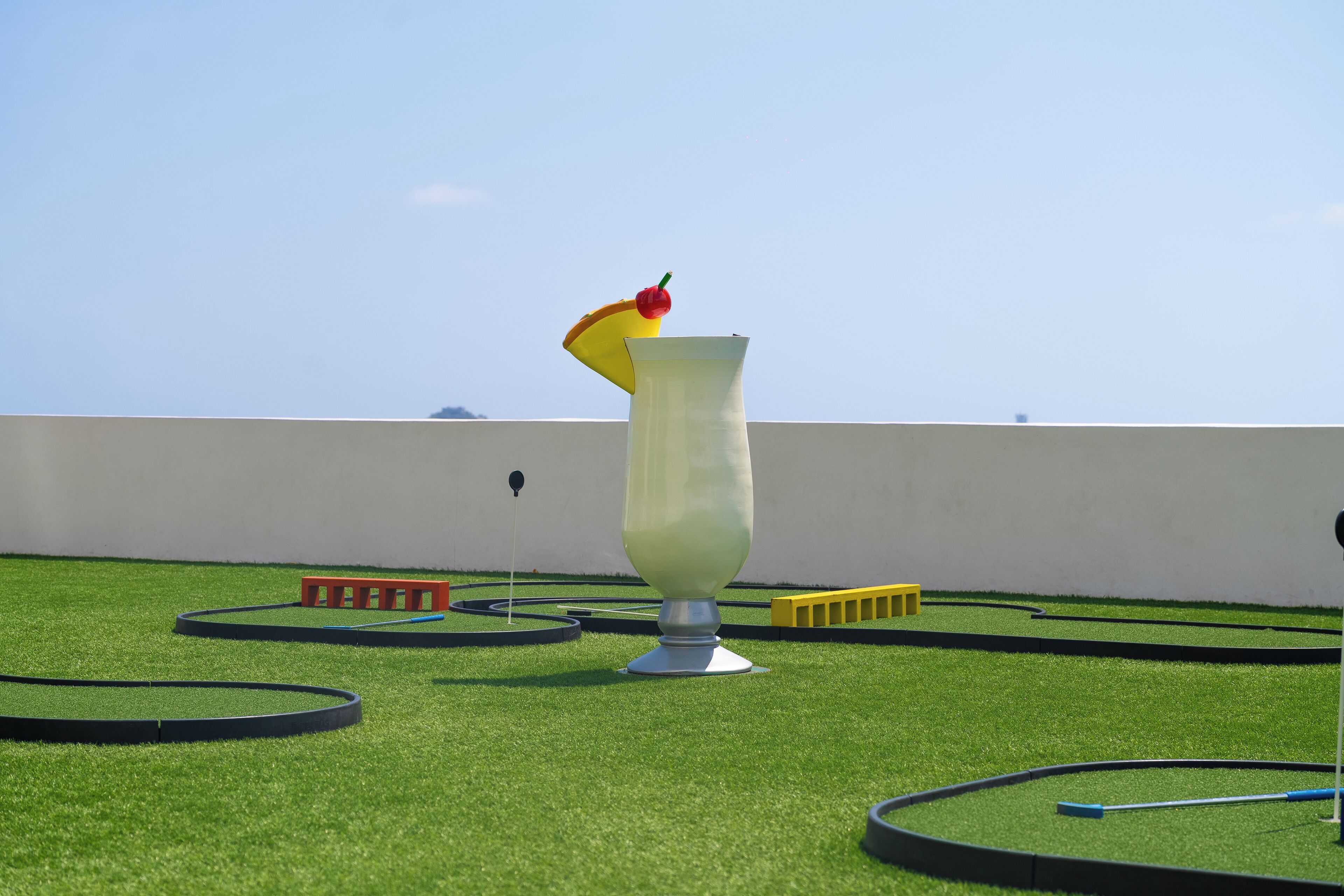 A virtual golf course with a large, white, abstract sculpture in the center, surrounded by green grass and various obstacles.