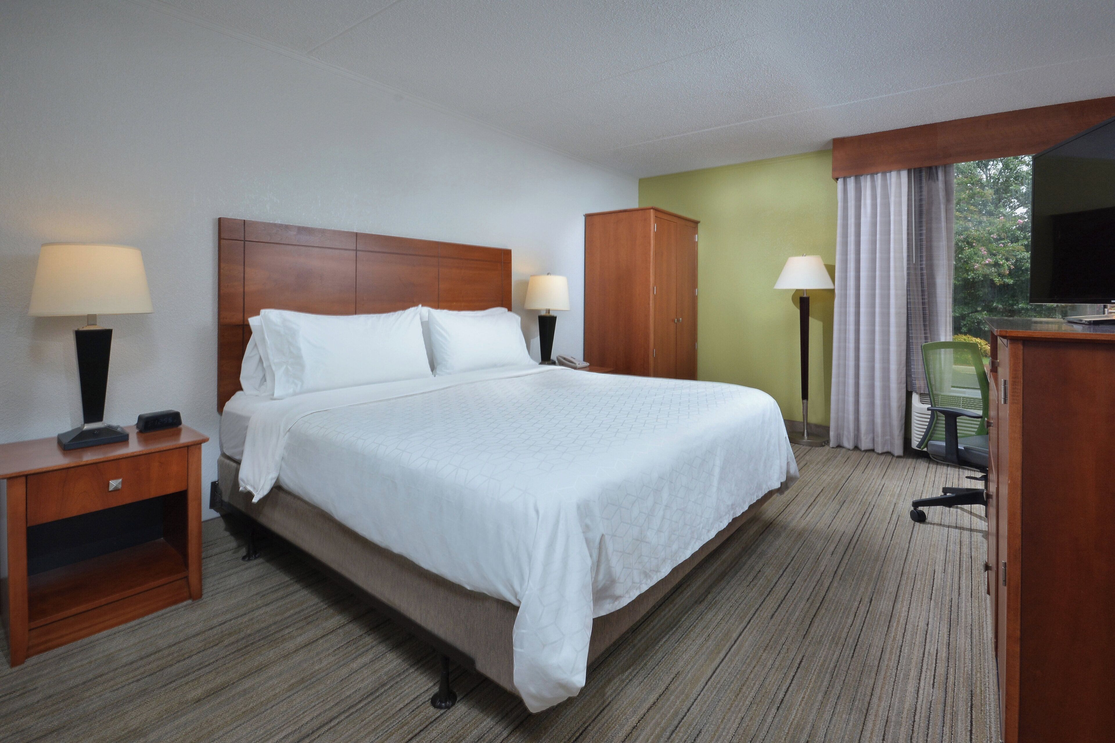 Een hotelkamer met een bed, bureau, kledingkast, stoel en televisie.