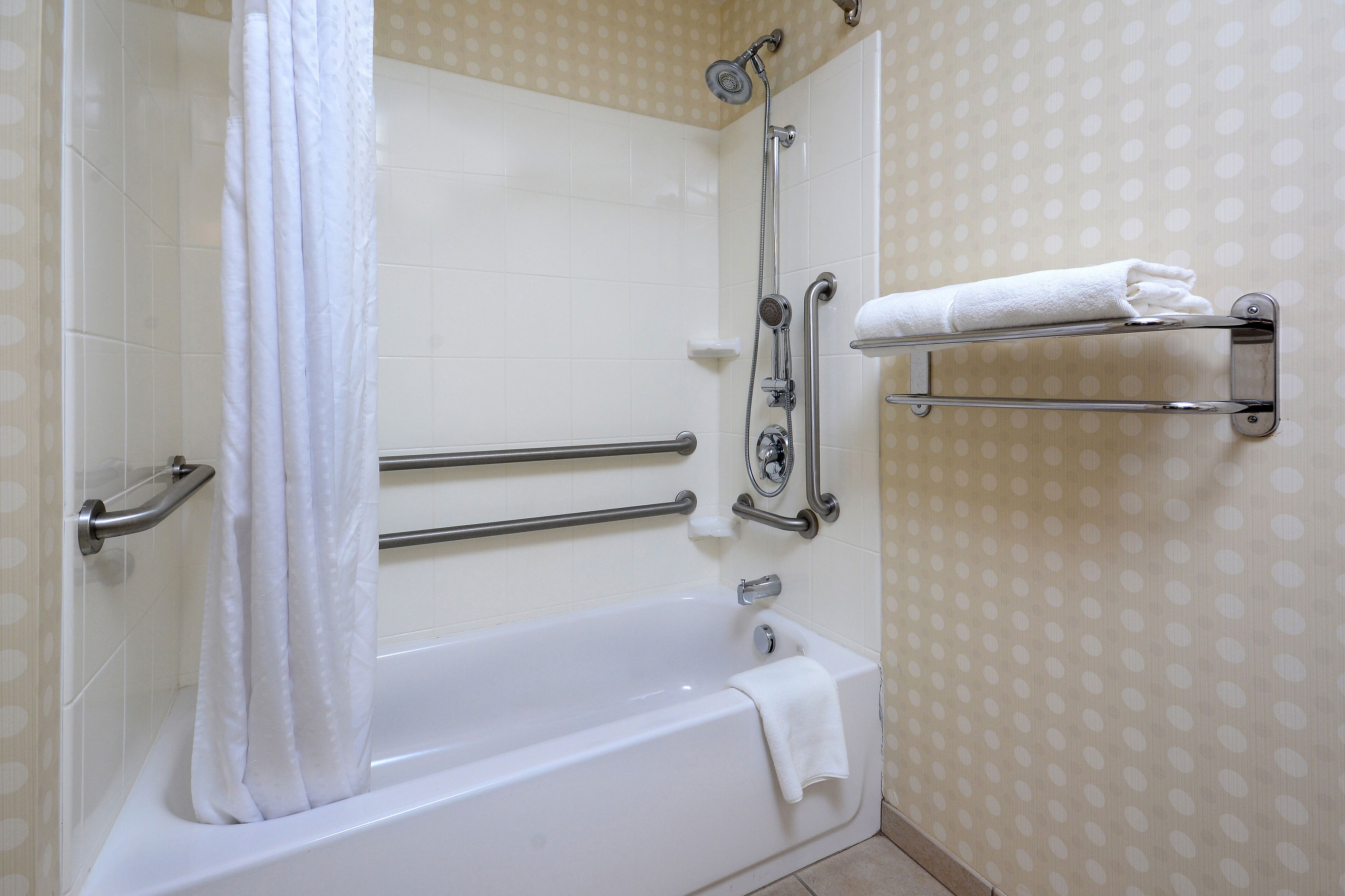 Ein Badezimmer mit einer Badewanne, Haltegriffen, einer Duschbrause und einem Handtuchhalter.