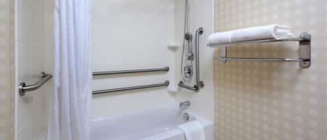 Un baño con bañera, barras de apoyo, cabezal de ducha y un perchero para toallas.