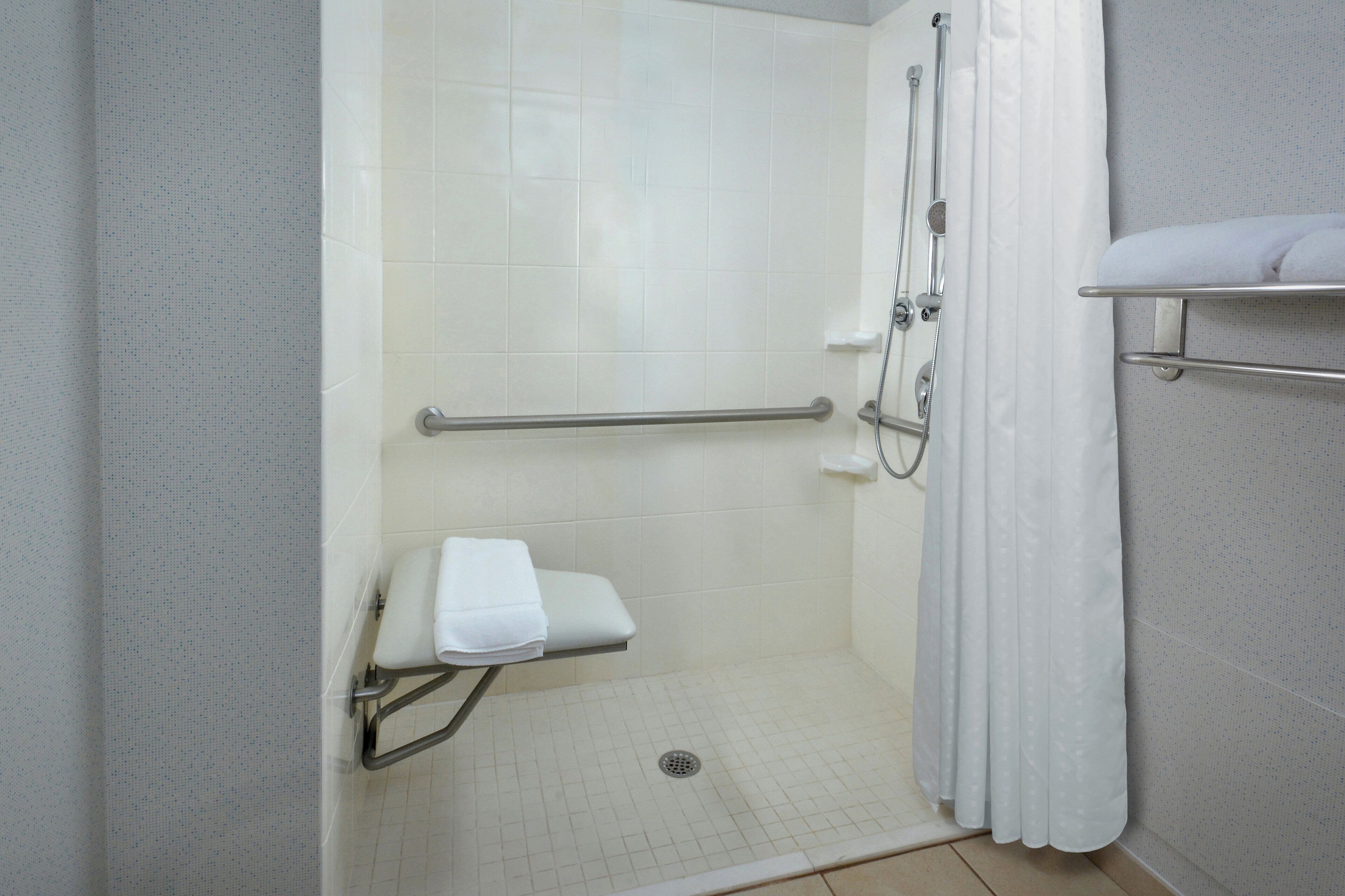 A walk-in shower with a grab bar, a white towel on a shelf, and a shower curtain.
