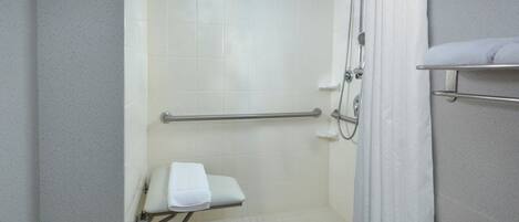 A walk-in shower with a grab bar, a white towel on a shelf, and a shower curtain.