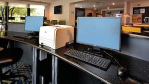 A modern office space with multiple workstations, each equipped with a desktop computer, keyboard, and monitor. There is a printer on the counter, and the room has large windows allowing natural light. - Holiday Inn Express Lynchburg by IHG (Lynchburg)