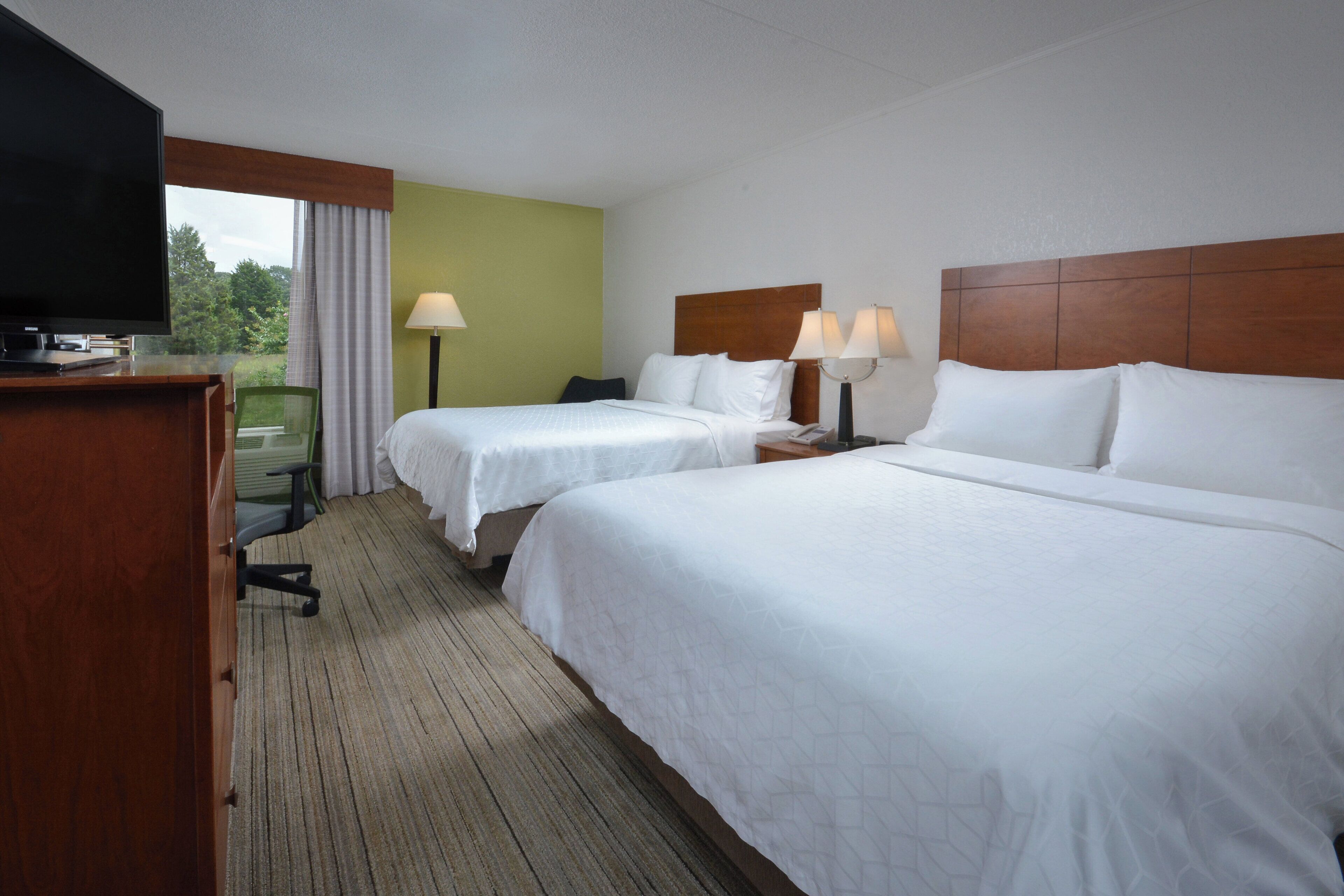Une chambre d’hôtel avec deux lits, un bureau avec une télévision et une vue sur l’extérieur.