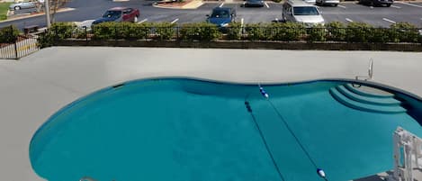 Una piscina con tabla de salto, rodeada por un estacionamiento con varios coches.
