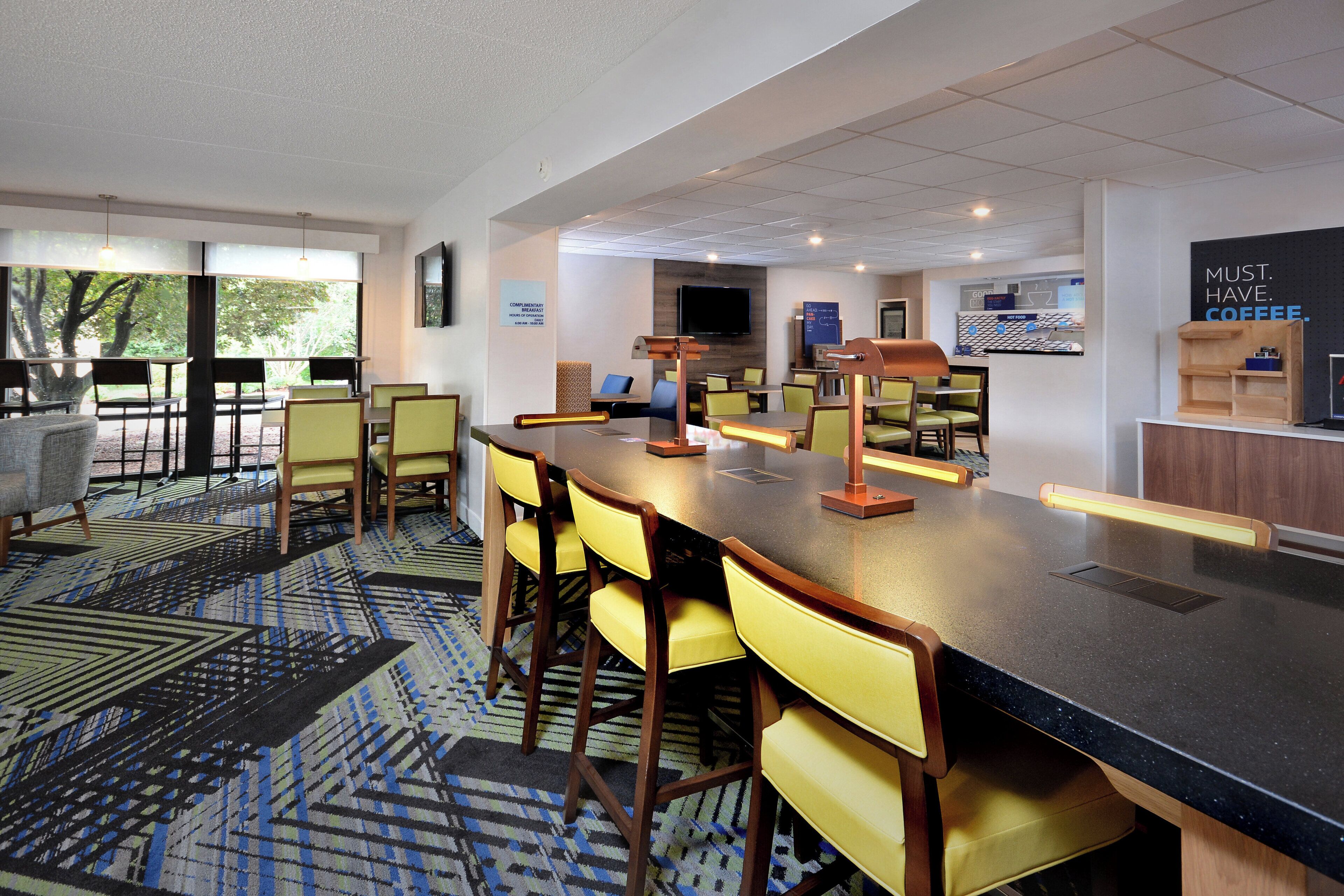 A modern bar area with a long counter, multiple chairs, and a television screen.